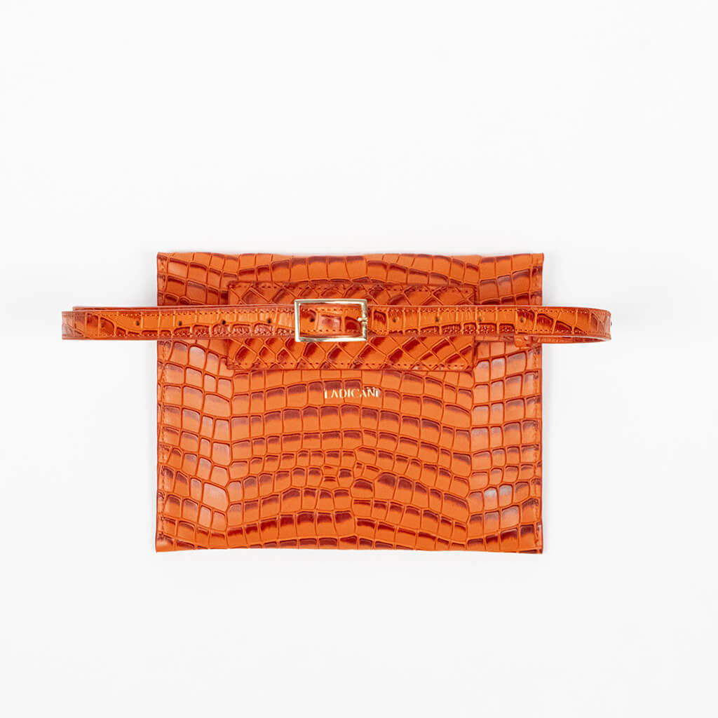 Back of an orange clutch bag with a strap on a white background