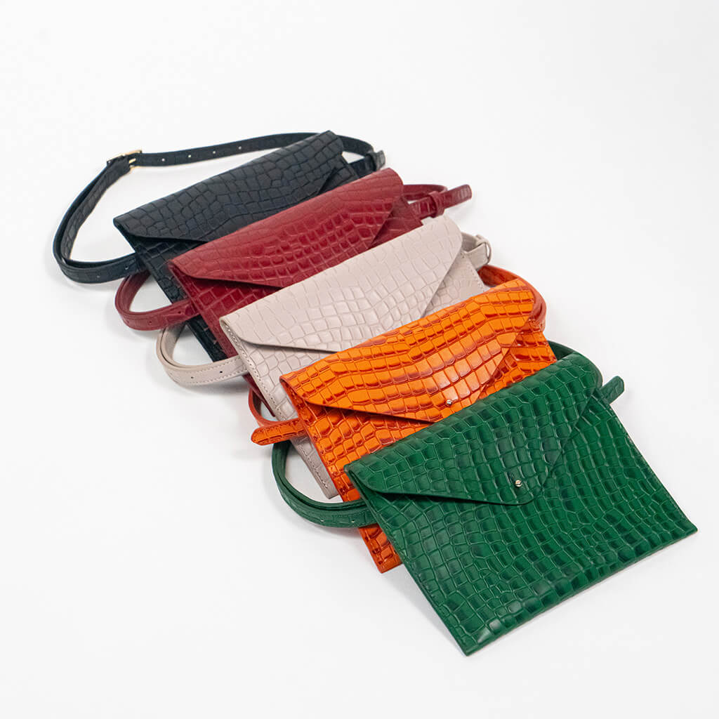 Five leather clutches in black, red, beige, orange, and green on a white background.