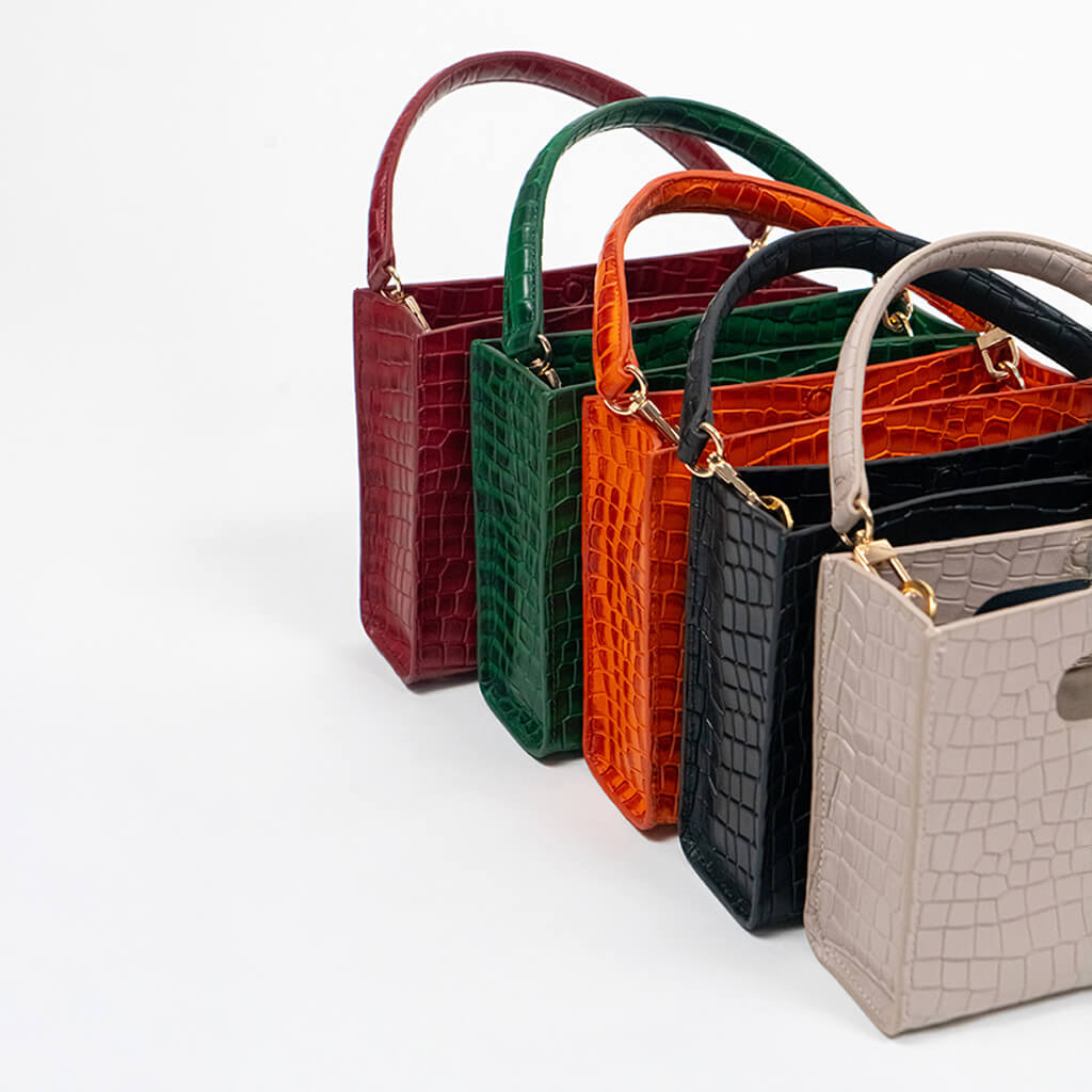 Set of five cassette bags in red, green, orange, black, and beige arranged in front of each other on a white background