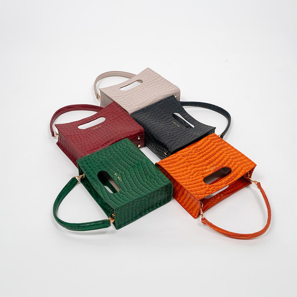 Set of five cassette bags in red, green, orange, black, and beige arranged in a staggered formation on a white background