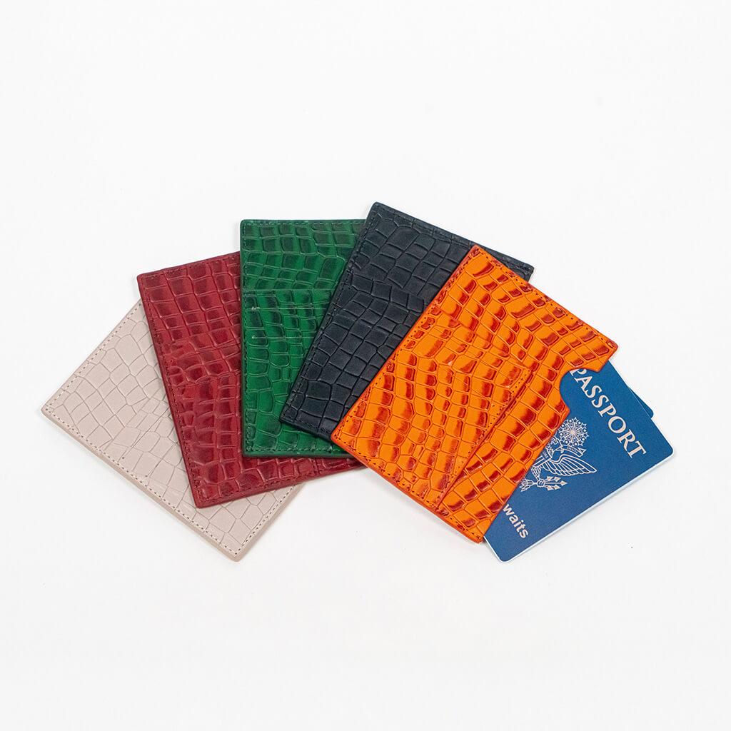 Five leather passport holders in different colors with a blue passport on a white background