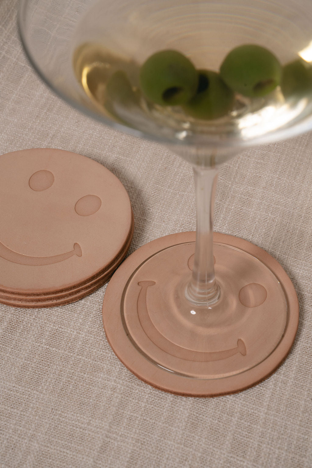 Smiley face leather coasters with a martini glass on a textured surface