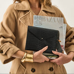 Woman holding a magazine and clutch with a plain background