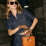 Woman in a denim outfit holding an orange handbag.