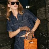 Woman in a denim outfit holding an orange handbag.