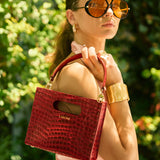 Woman holding a red handbag with a blurred green background