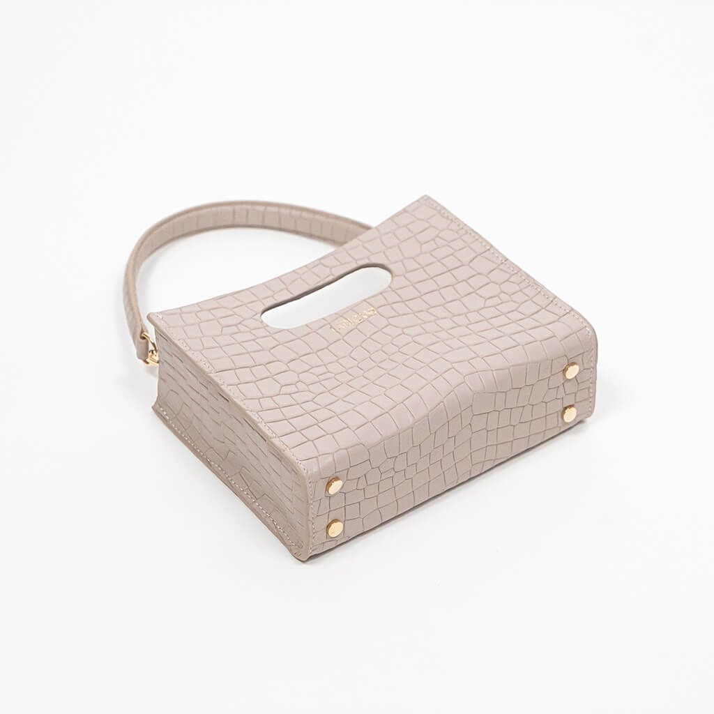 Beige textured cassette bag with a visible brand logo and strap laying down on a white background