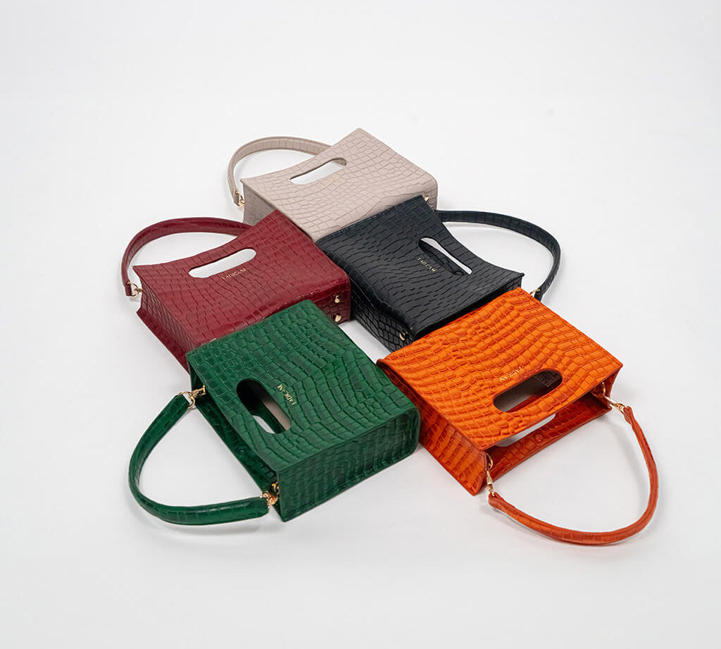 Set of five cassette bags in red, green, orange, black, and beige arranged in a staggered formation on a white background