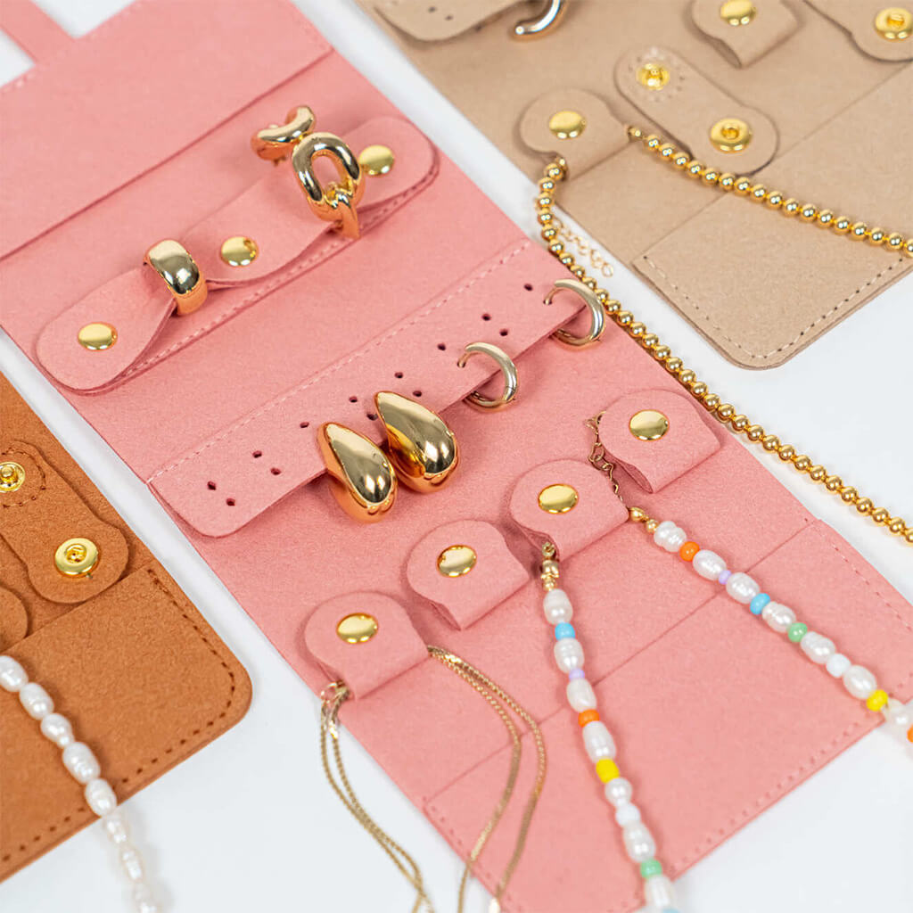 Closeup of a pink jewelry roll with gold jewelry and colorful beaded chains on a white background