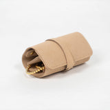 Closed beige leather jewelry roll with gold jewelry on a white background