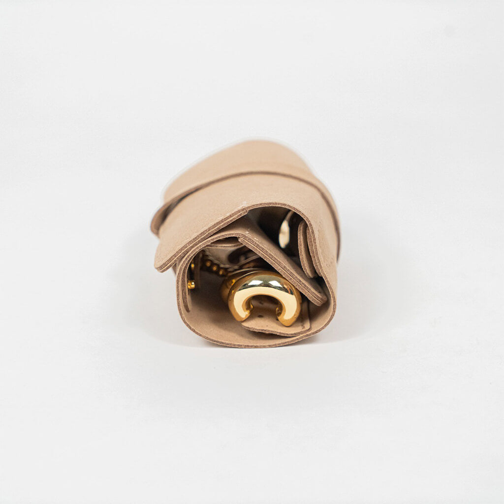 Closed beige leather jewelry roll with gold jewelry on a white background, side view