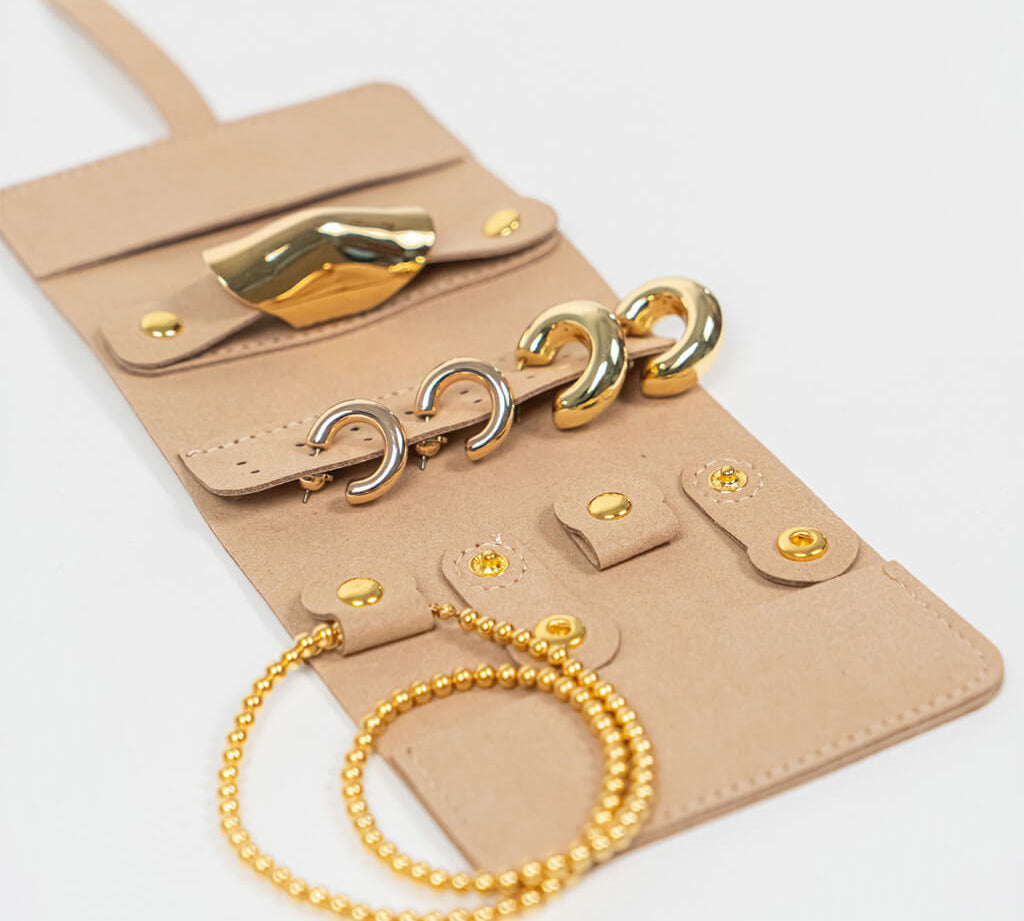 Beige leather jewelry roll with gold jewelry on a white background