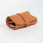 Closed brown leather jewelry roll with gold jewelry on a white background