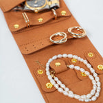 Closeup of a brown leather jewelry roll with gold jewelry on a white background