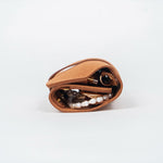 Closed brown leather jewelry roll with gold jewelry on a white background, side view