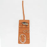 Open view of a brown leather jewelry roll with gold jewelry on a white background