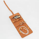 Brown leather jewelry roll with gold jewelry on a white background