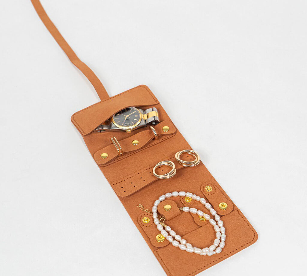 Brown leather jewelry roll with gold jewelry on a white background