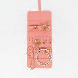 Front view of a pink leather jewelry roll with gold jewelry on a white background