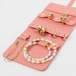 Closeup of a pink leather jewelry roll with gold jewelry on a white background
