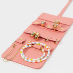 Pink leather jewelry roll with gold jewelry on a white background