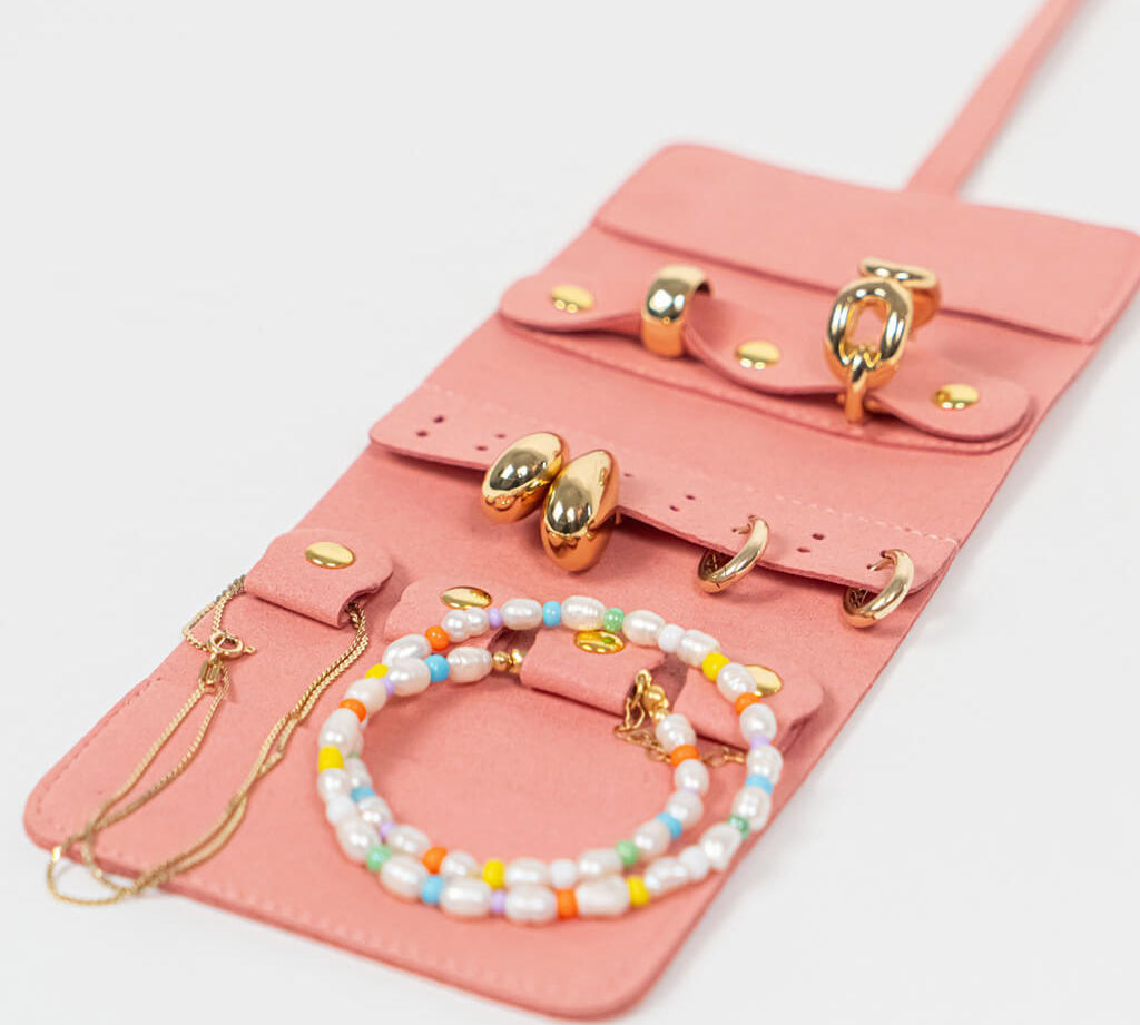 Pink leather jewelry roll with gold jewelry on a white background
