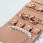 Closeup of a light pink leather jewelry roll with gold jewelry on a white background