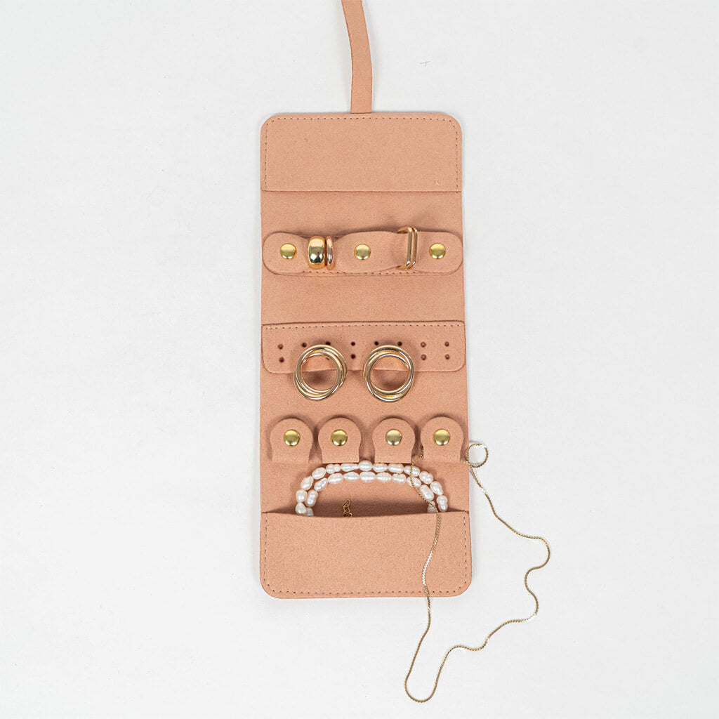 Open view of a light pink leather jewelry roll with gold jewelry on a white background
