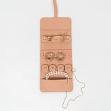 Open view of a light pink leather jewelry roll with gold jewelry on a white background