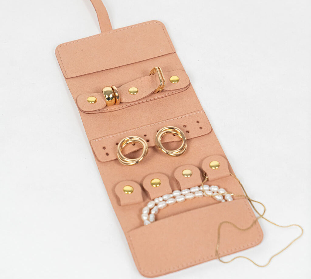 Light pink leather jewelry roll with gold jewelry on a white background
