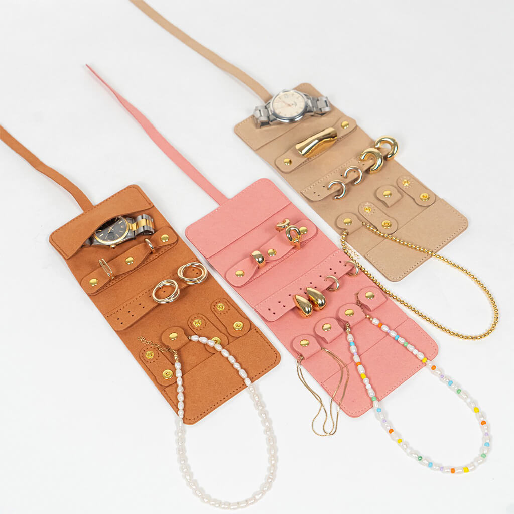 Three leather jewelry rolls in brown, pink, and beige with accessories on a white background