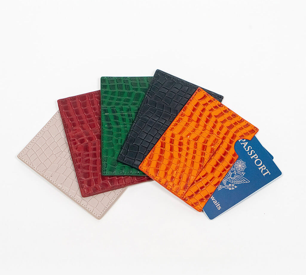Five leather passport holders in different colors with a blue passport on a white background