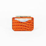 Orange leather slim wallet with money, a card, and branding on a white background