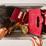Red handbag with sunglasses, passport cover and cardholder on a gray surface
